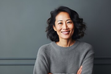 Fototapeta premium Portrait of happy young Asian woman with arms crossed against grey background