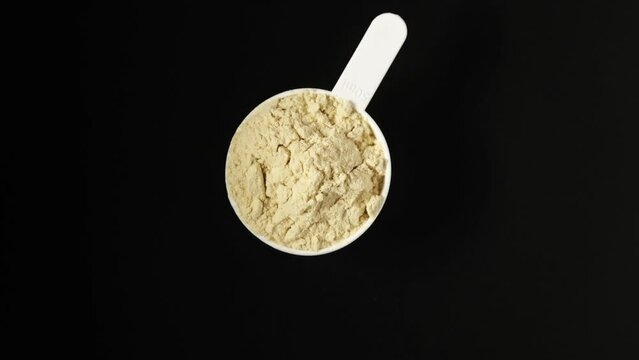Soy protein concentrate, isolated from soybean in plastic measuring spoon, top view. Pure Whey Protein. Video, 4K. Rotating. Food additive, ingredient for fitness cocktail or smoothie.