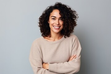 Portrait of a smiling young woman standing with arms crossed over gray background
