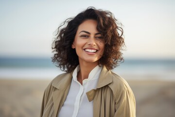 smiling young woman in beige jacket looking at camera on beach