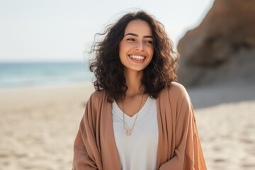 cheerful young woman in beige coat smiling at camera on beach