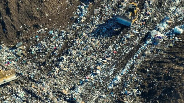 View from above of landfill dump site for garbage waste managment. Bulldozer tractors burying large amount of trash under the ground. Harmful impact of modern consumerism on environment