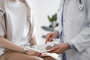 Doctor and patient in clinic. Friendly physician using tablet computer near a young woman. Medicine concept
