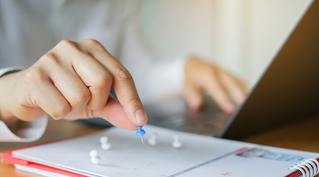 close hand use pushpin on calendar to booking about date and time of meeting for day off vacation or important appointments for lifestyle concept