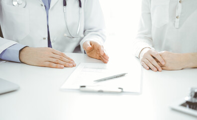 Doctor and patient discussing current health questions while sitting near of each other at the table in clinic, just hands closeup. Medicine concept