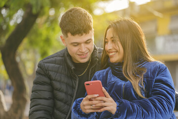 Smiling girl showing her mobile phone to a boy in a public park.