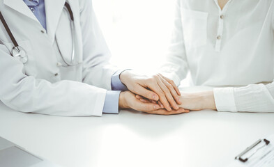 Doctor and patient sitting near each other at the table in clinic office. The focus is on female physician's hands reassuring woman, only hands, close up. Medicine concept