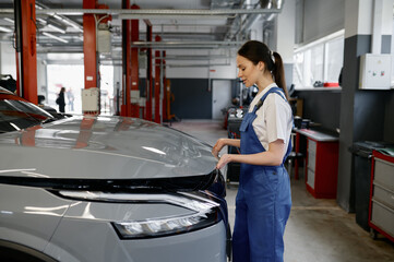 Fototapeta na wymiar Young woman car mechanic looking under hood while working at repair garage