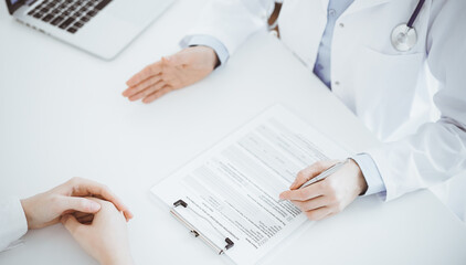 Doctor and patient discussing current health questions while sitting opposite of each other and using clipboard at the table in clinic, just hands closeup. Medicine concept