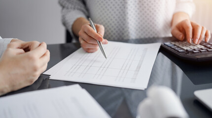 Woman accountant using a calculator and laptop computer while counting and discussing taxes with a client. Business audit and finance concepts