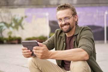 Mid-aged, handsome man sitting on the stairs of an embankment, engrossed in reading good news on...