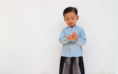 Obraz na płótnie Canvas A cute little boy with blue shirt and sarong praying