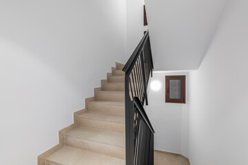 Beautiful comfortable staircase with a beige track, black metal railings and white walls in a new...