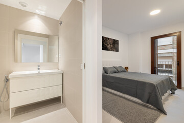Fototapeta na wymiar Light, minimalist bathroom with sink, cabinet and mirror in the bathroom with an open door to the bedroom with double bed. Concept of comfortable compact apartment after renovation