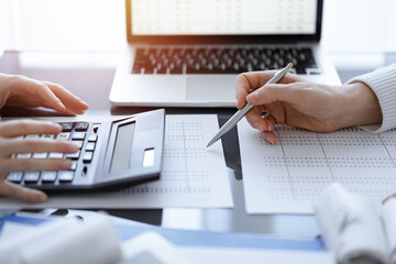 Woman accountant using a calculator and laptop computer while counting taxes for a client. Business audit concepts - 623786180
