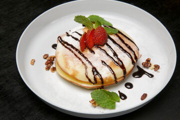 
Thick and fluffy American pancakes drenched in chocolate syrup with fresh strawberries and mint leaf