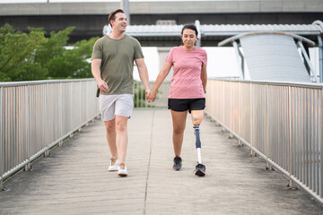 Exercise Asia woman with prosthetic leg holding hand caucasian boy friend in the park city	