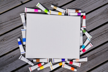 Background blank white canvas with tubes of colored paints on wooden