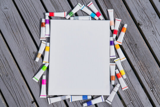 Background blank white canvas with tubes of colored paints on wooden