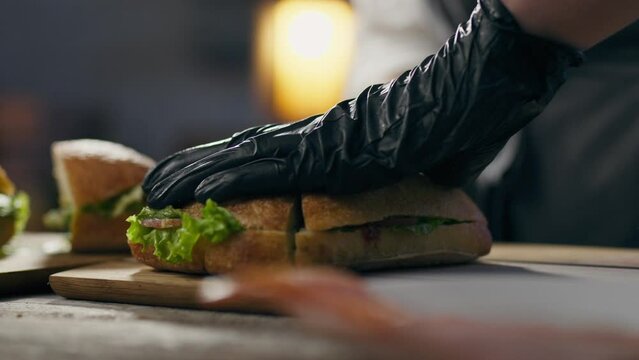 Cooking, cooking master Cuts a crispy sandwich with a knife in an authentic sandwich bar. close-up of a fast food chef preparing food for customers showing his skill in making food, delivering
