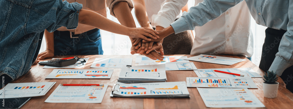 Aufkleber Analyst team putting hand together after successfully analyzed financial dashboard papers for business strategy and marketing. Teamwork and unity in office with stack hands. Panorama shot. Scrutinize