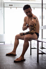 An adult swimmer with an amputated arm is putting on his arm prosthesis sitting in a changing room in a heated indoor pool. Concept of disabled athletes, inclusive sport. Motivation and overcoming.