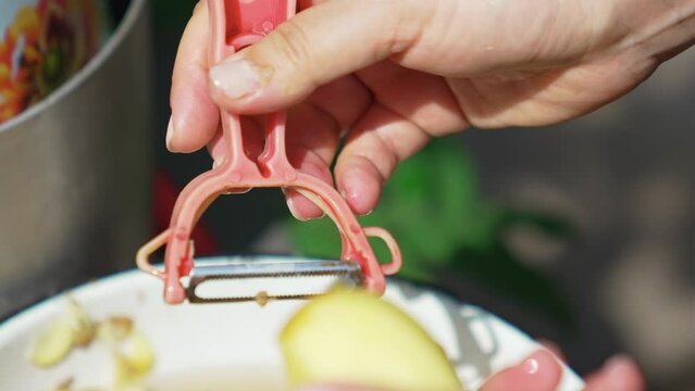 Women's hands peel potatoes with a vegetable peeler. 