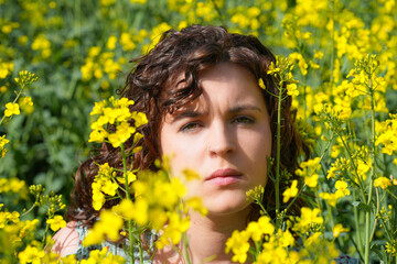 Junge Frau blickt nachdenklich aus einem blühenden Feld in die Kamera