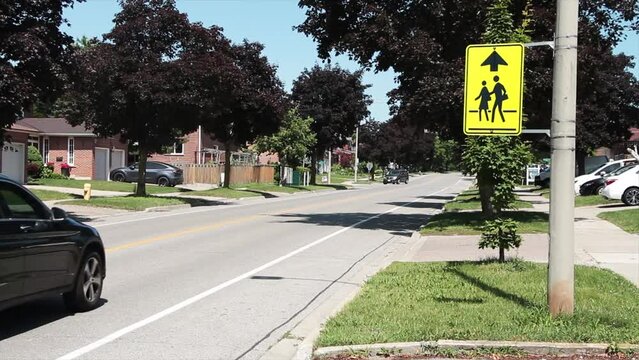 wide on neon yellow school zone sign in black with up arrow next to long residential street with vehicles passing in background