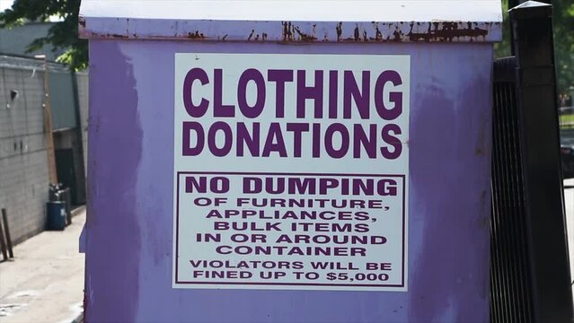 large light purple metal bin with sign that says clothing donations no dumping of furniture, appliances, bulk items in or around container violators will be fined up to $5,000, slide movement