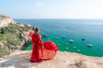 Red Dress Woman sea Cliff. A beautiful woman in a red dress and white swimsuit poses on a cliff overlooking the sea on a sunny day. Boats and yachts dot the background.