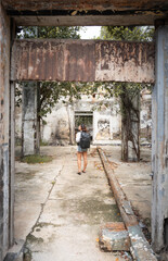 Plakat traveling girl in white shirt and black backpack discovering the ruins of a house