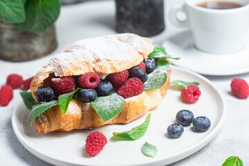 Croissant with raspberries, blueberries and cream cheese on a white plate
