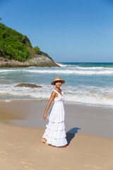 Fototapeta na wymiar A woman exudes elegance and happiness as she walks on the beach in a white dress, embracing the coastal beauty with a radiant smile.