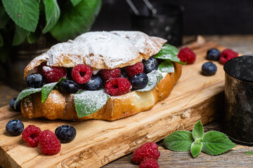 Croissant with raspberries, blueberries and cream cheese on a wooden board