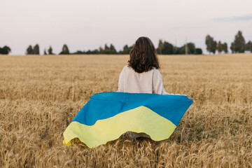 A Ukrainian girl in a dress walks holding a freely waving flag in a middle of the golden wheat crop...