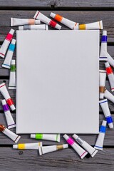 Background blank white canvas with tubes of colored paints on wooden
