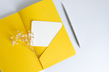 open yellow notebook with a pen on a white background with flowers. gentle composition of postcard, letter and inspiration.	