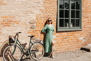 Fototapeta na wymiar Kobieta w zielonej sukience oraz z zielonym rowerem stoi pod ceglaną ścianą w Gdańsku