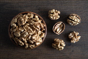 Peeled walnuts and whole walnuts in wooden bowl,top view
