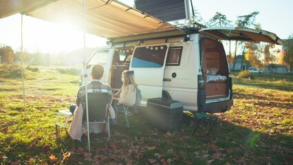 Young couple enjoying beautiful sunset having picnic in the forest near the camping bus. Traveling people lifestyle. Sunny background. Happy marriage rests outdoors. - Powered by Adobe