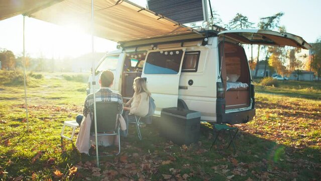Young couple enjoying beautiful sunset having picnic in the forest near the camping bus. Traveling people lifestyle. Sunny background. Happy marriage rests outdoors.