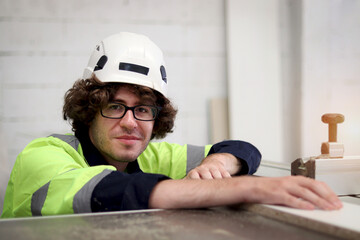 Happy industrial worker man wearing glasses, helmet and safety vest, working and inspecting wood raw material, male engineer working with automatic robot machinery at CNC woodworking furniture factory