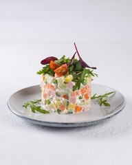 New Year. Olivier salad on a plate with tomatoes and arugula.