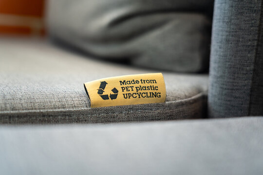 "PET Plastic upcycling" product label tag on the sofa seat fabric material part. Sign and symbol object photo, selective focus.