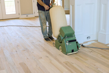 Carpenter grinding wooden parquet floor by using floor sander an newly constructed house