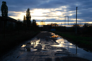 Puddles on a broken rural road at sunset. Late evening.