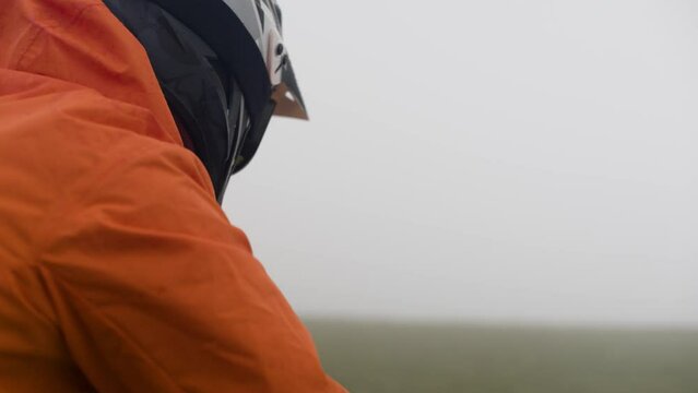 Portrait from the back of a mtb cyclist rider in an orange jacket and full face helmet and goggles looks into the distance outdoors and turns to the camera
