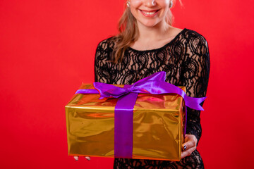 Portrait of an attractive young woman in a black dress with a gift in her hands, isolated on a red background.