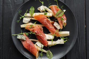 Appetizer of prosciutto, pear and blue cheese on a black plate for the holiday, close-up, top view